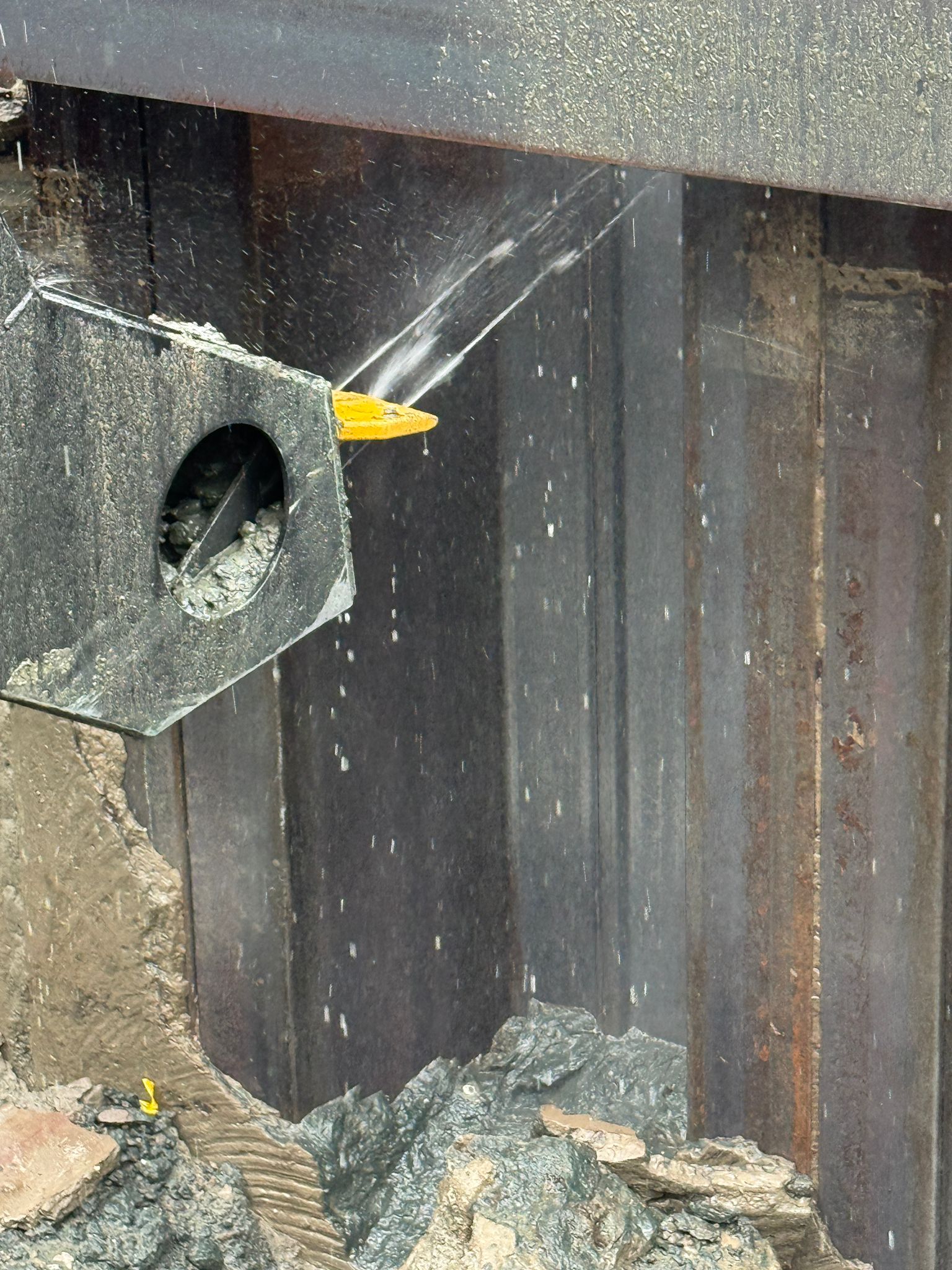 Hompert-Renes - Damwand reinigen | Hompert - Renes Yellow wedge tool sticking out from a black metal frame at a construction site with rubble on the ground